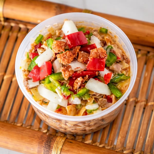 Filipino sisig in a clear plastic container, with red and green bell peppers, onions, and pork cracklings.