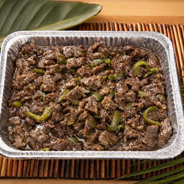 Filipino beef salpicao with green peppers in a foil tray on a bamboo mat.