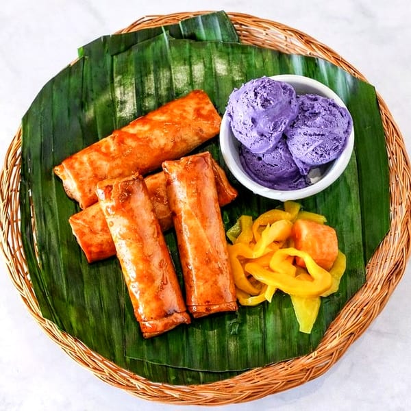 Filipino dessert platter with fried banana rolls, purple ube ice cream, and jackfruit on banana leaves.