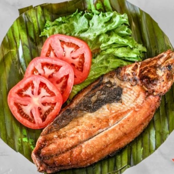 Grilled fish served on a banana leaf with fresh lettuce and sliced tomatoes.