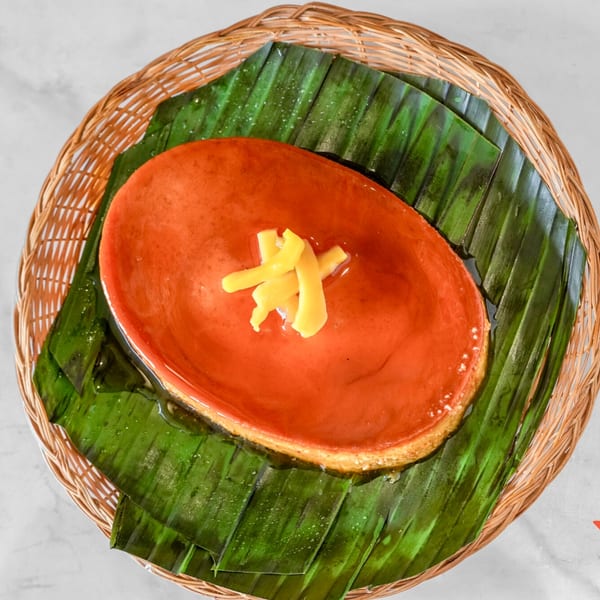 Overhead view of a flan dessert with ginger slivers, served on banana leaves in a woven basket.
