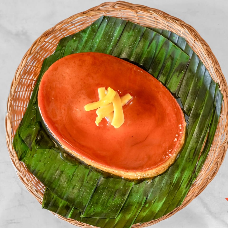 Overhead view of a flan dessert with ginger slivers, served on banana leaves in a woven basket.