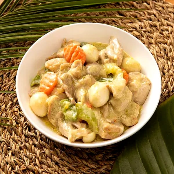 Filipino Ginataang Manok, chicken in coconut milk with vegetables and quail eggs, in a white bowl.